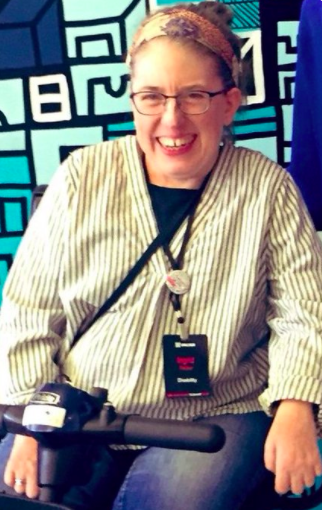 Woman in white cardigan and lanyard sitting in a wheelchair